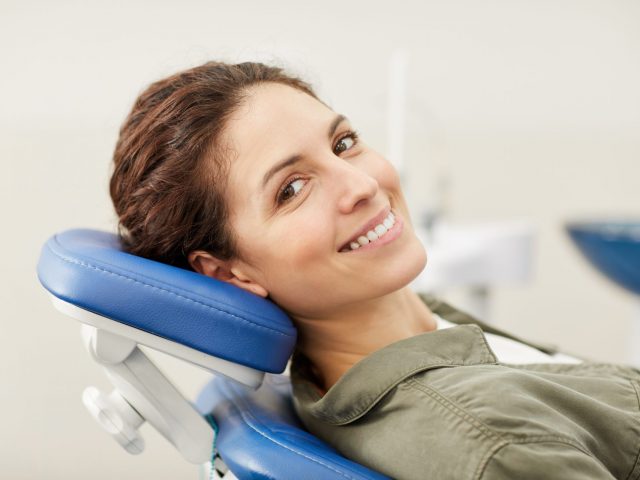 Portrait of smiling young woman lying in dental chair and looking at camera, copy space